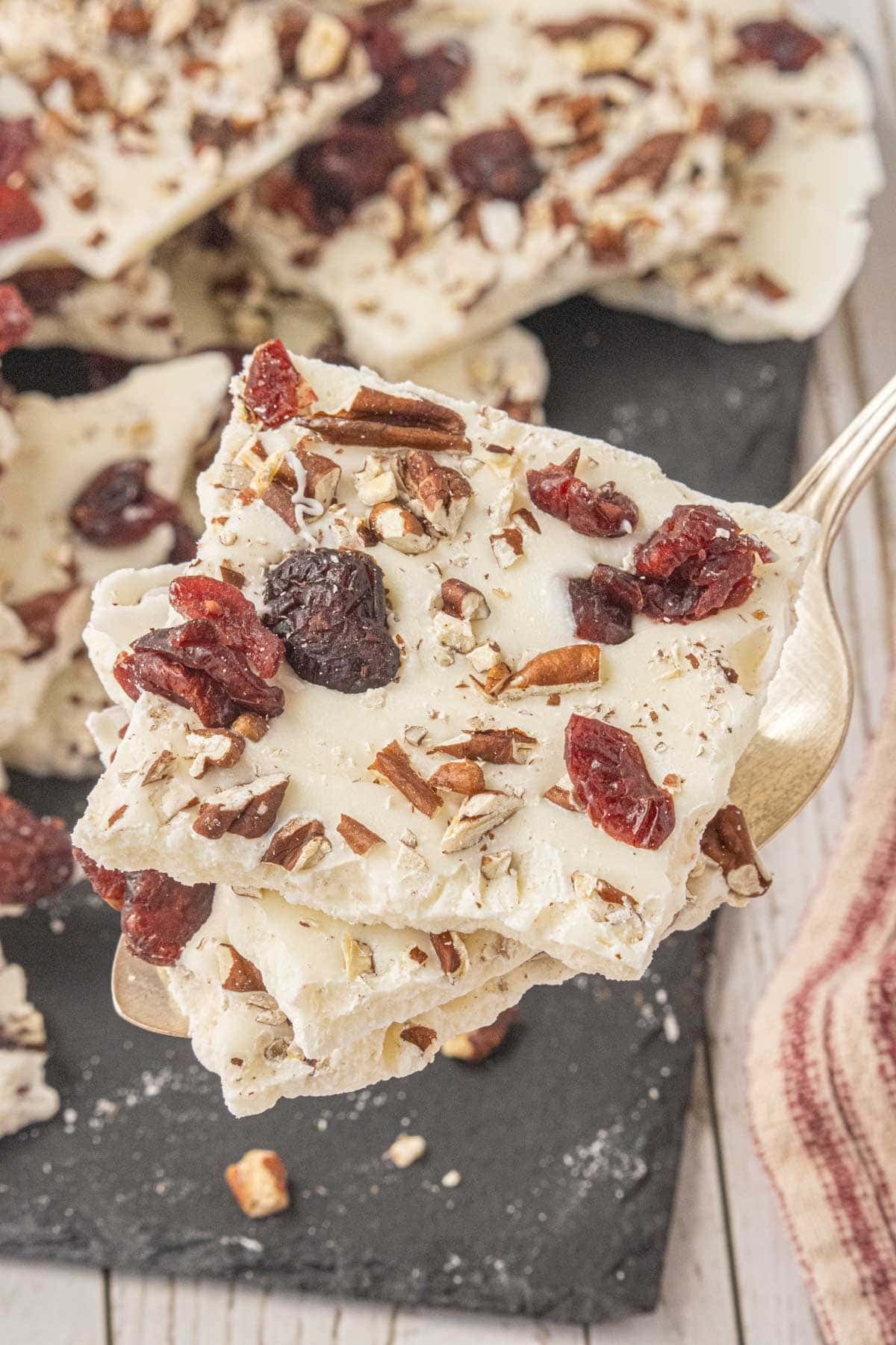 Close-up of white chocolate cranberry bark topped with dried cranberries and chopped pecans on a serving spoon.