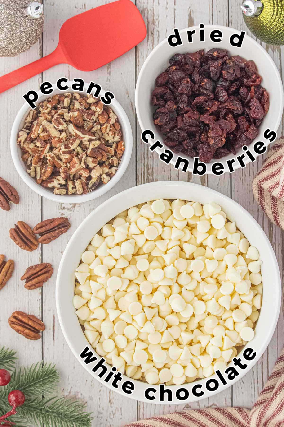 Ingredients for white chocolate cranberry bark including white chocolate chips, chopped pecans, and dried cranberries.