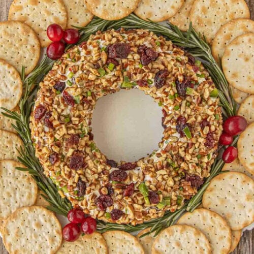 Cranberry cheese ball wreath surrounded by crackers, rosemary sprigs, and fresh cranberries.