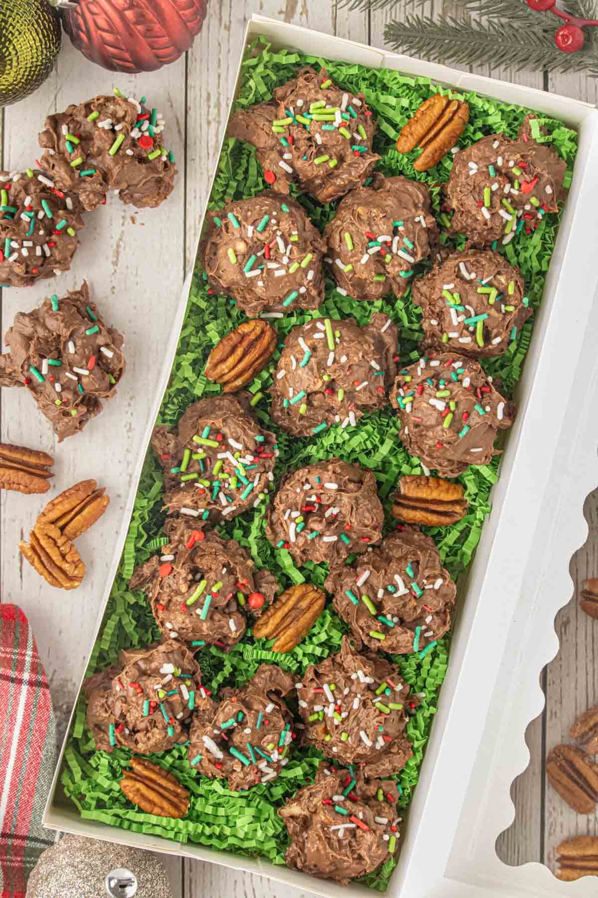 Holiday gift box filled with homemade crockpot candy nestled in green paper shred and decorated with pecans and Christmas sprinkles.