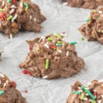 Pieces of homemade crockpot candy on parchment paper decorated with red, green, and white Christmas sprinkles.