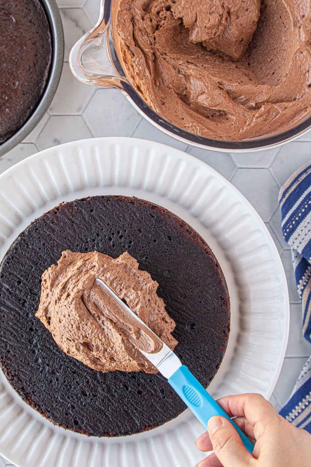 Offset spatula spreading chocolate fudge frosting onto a dark chocolate cake layer.