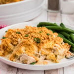 Plated serving of creamy hash brown chicken casserole with crispy cornflake topping and green beans on a white dinner plate.