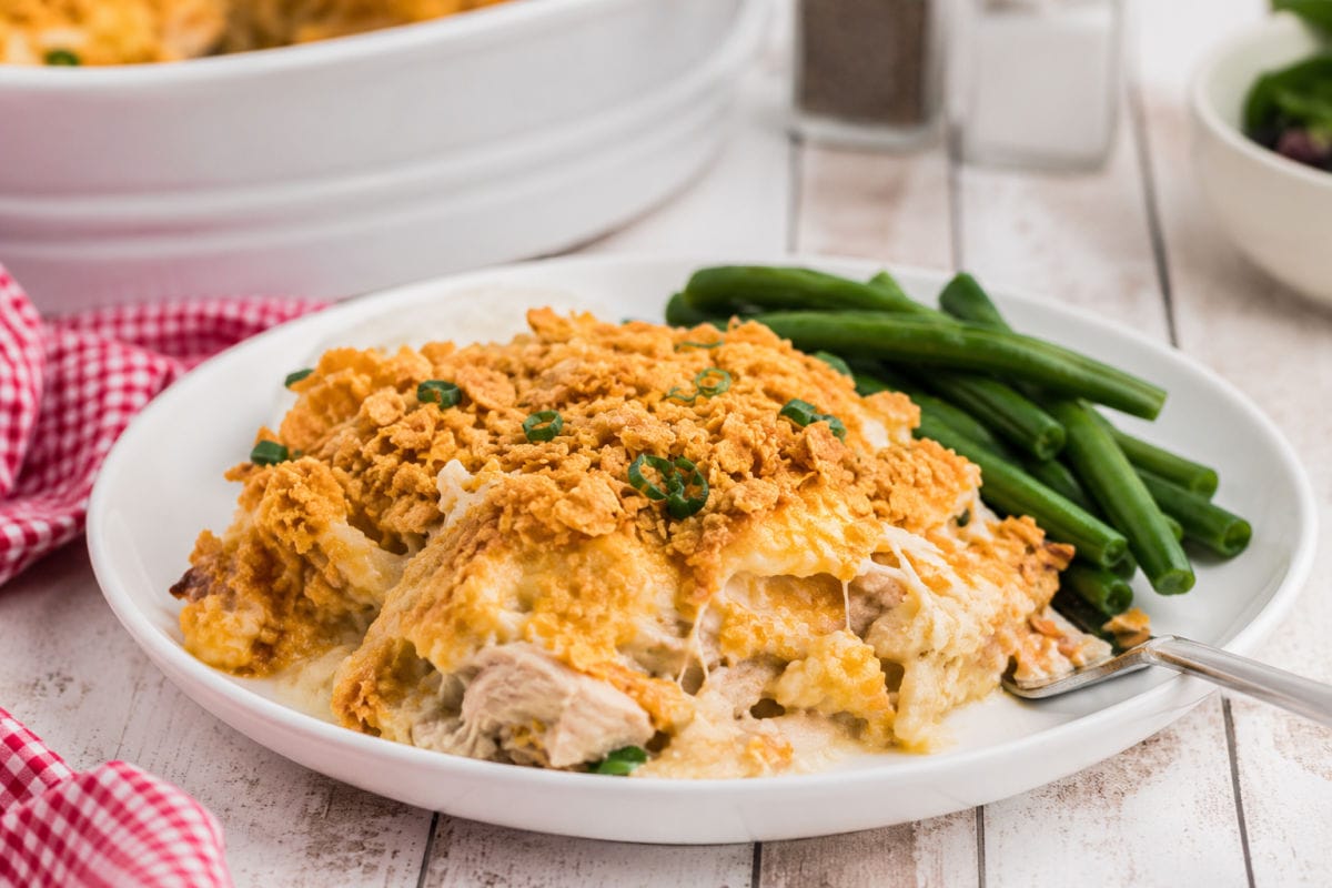 Plated serving of creamy hash brown chicken casserole with crispy cornflake topping and green beans on a white dinner plate.