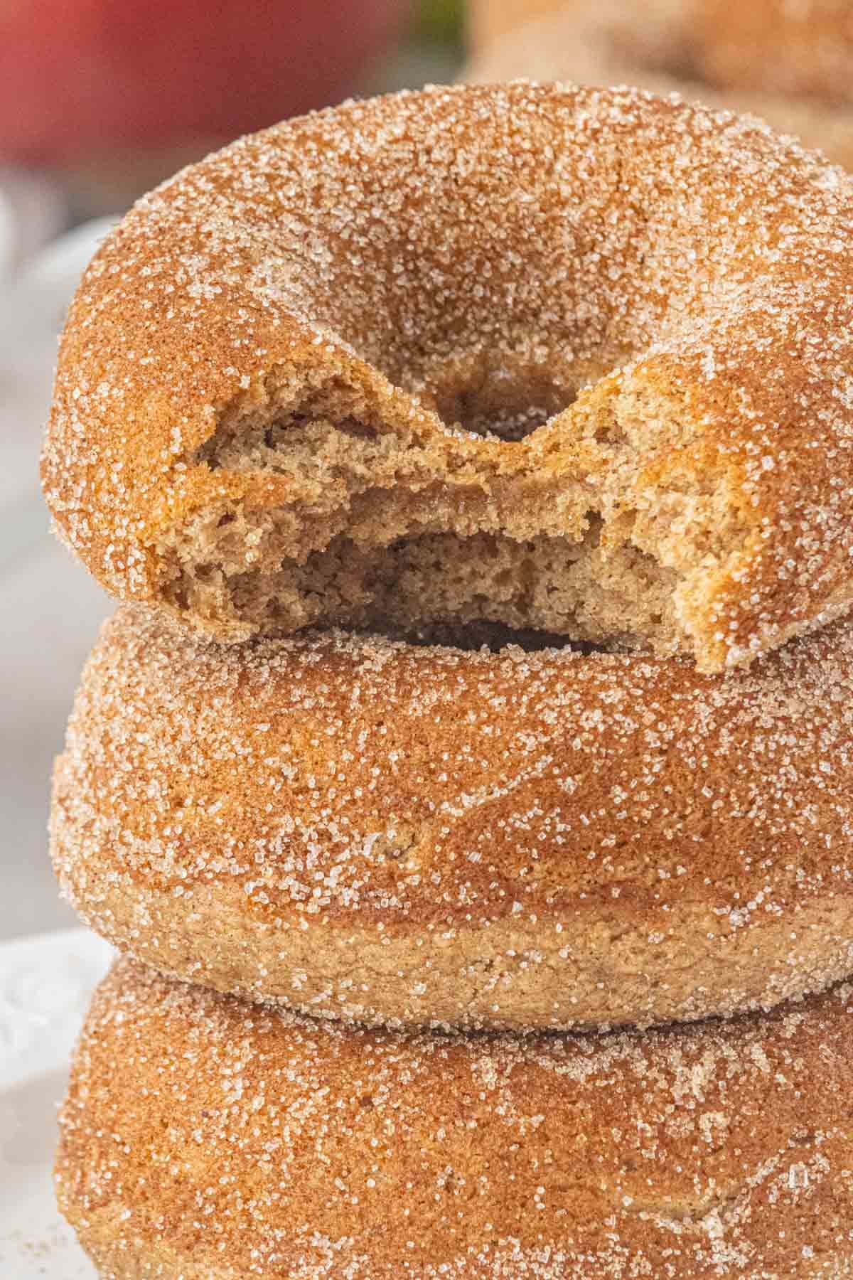 Bitten baked apple cider donut coated in cinnamon sugar and stacked with two more donuts.