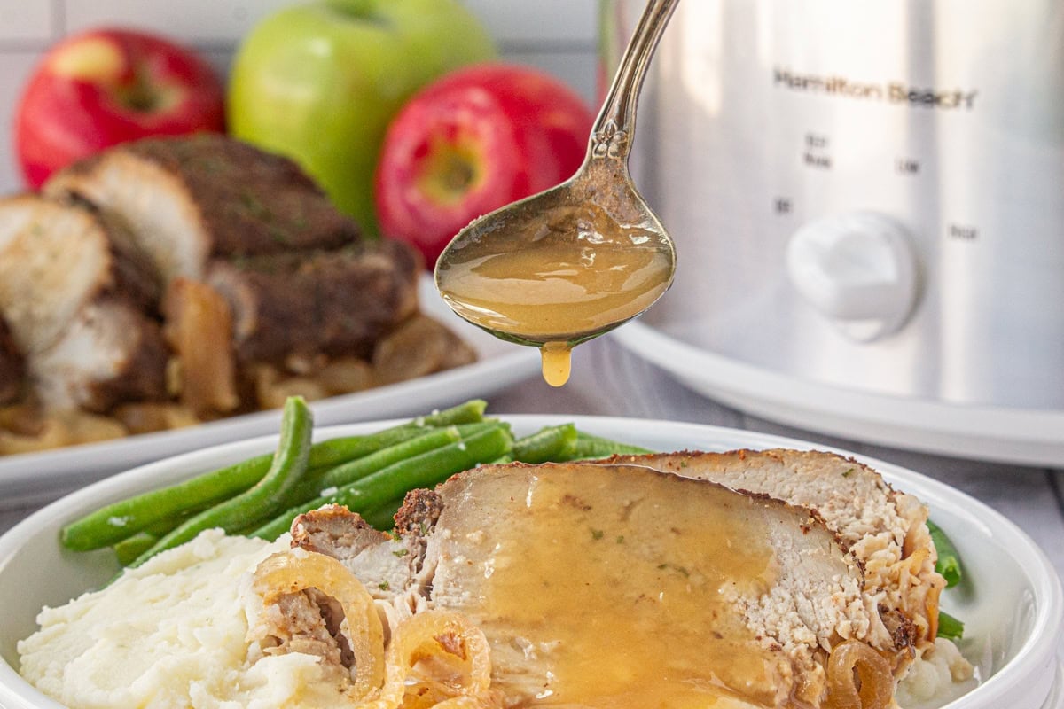 Slow cooker apple cider pork loin roast being drizzled with apple cider sauce.