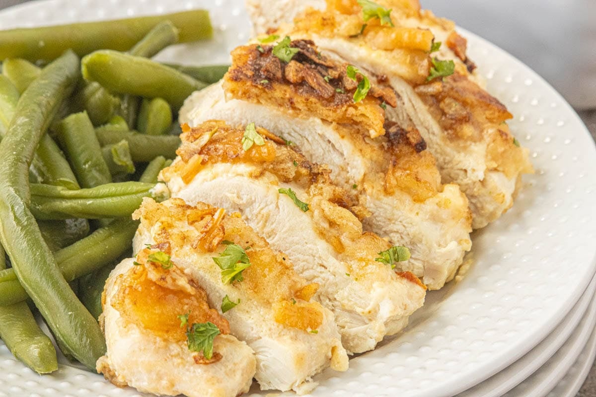 Ritz chicken sliced on a white plate with green beans and crispy golden cracker topping
