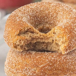 Bitten baked apple cider donut coated in cinnamon sugar and stacked with two more donuts.