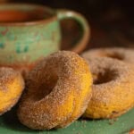 Cinnamon sugar pumpkin donuts made with cake mix beside a rustic coffee mug