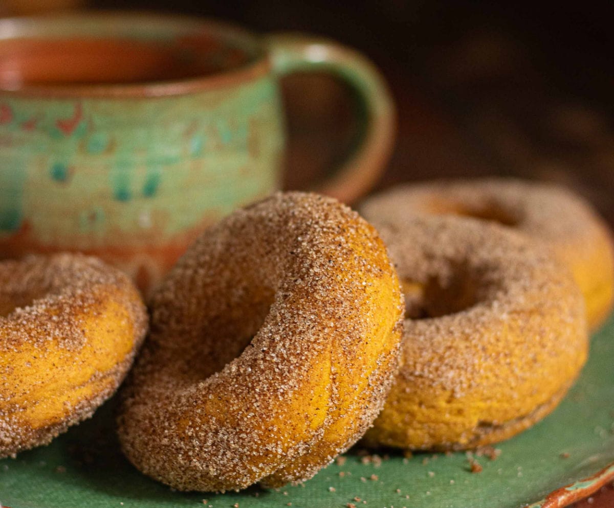 Cinnamon sugar pumpkin donuts made with cake mix beside a rustic coffee mug