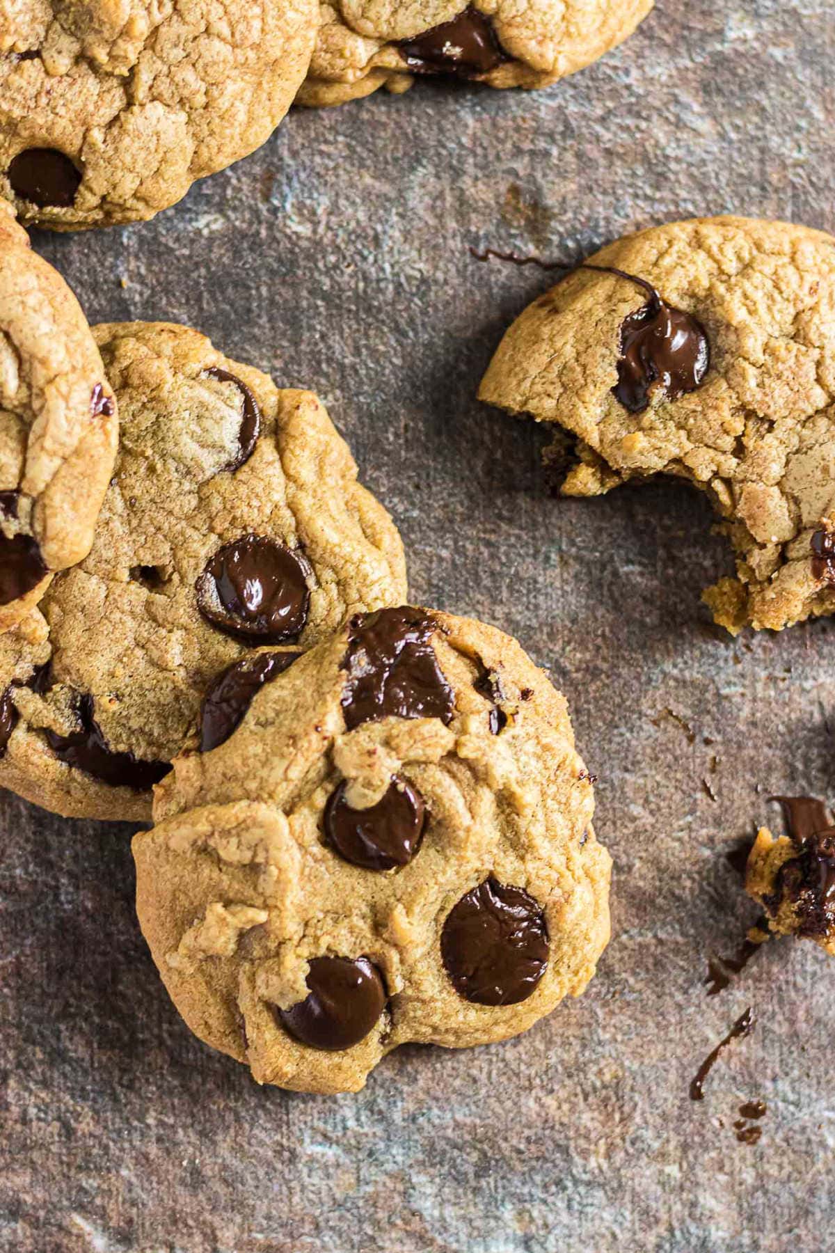 Brown butter chocolate chip cookies with melted chocolate chips scattered on a dark baking surface.