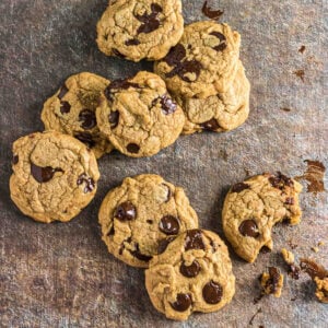 Freshly baked brown butter chocolate chip cookies scattered on a dark textured surface.