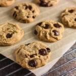 Fresh brown butter chocolate chip cookies cooling on parchment paper over a wire rack.