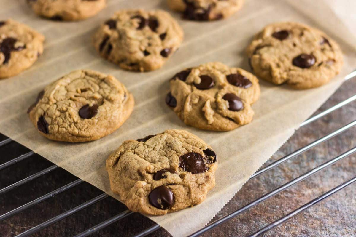 Fresh brown butter chocolate chip cookies cooling on parchment paper over a wire rack.