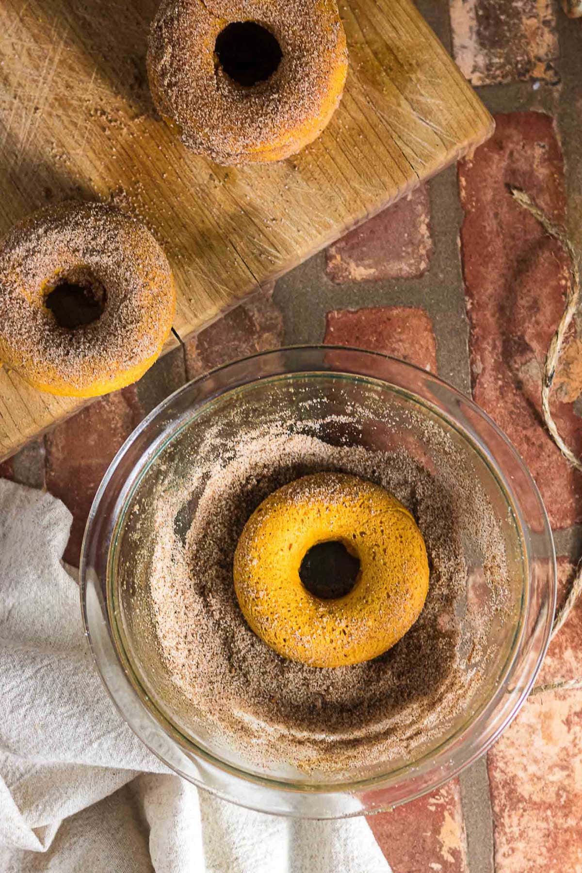 Baked pumpkin donut being coated in cinnamon sugar