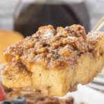 Thick slices of praline French toast casserole stacked on a plate with pecans and maple syrup.