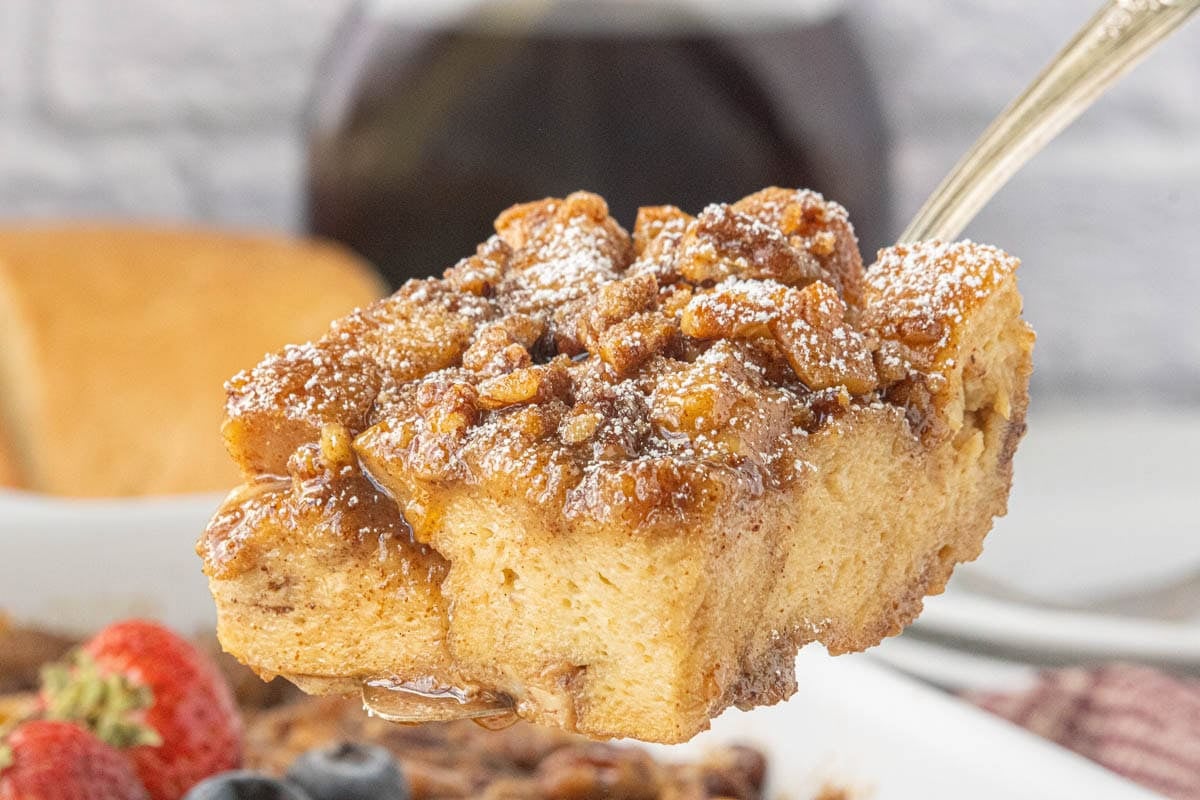 Thick slices of praline French toast casserole stacked on a plate with pecans and maple syrup.
