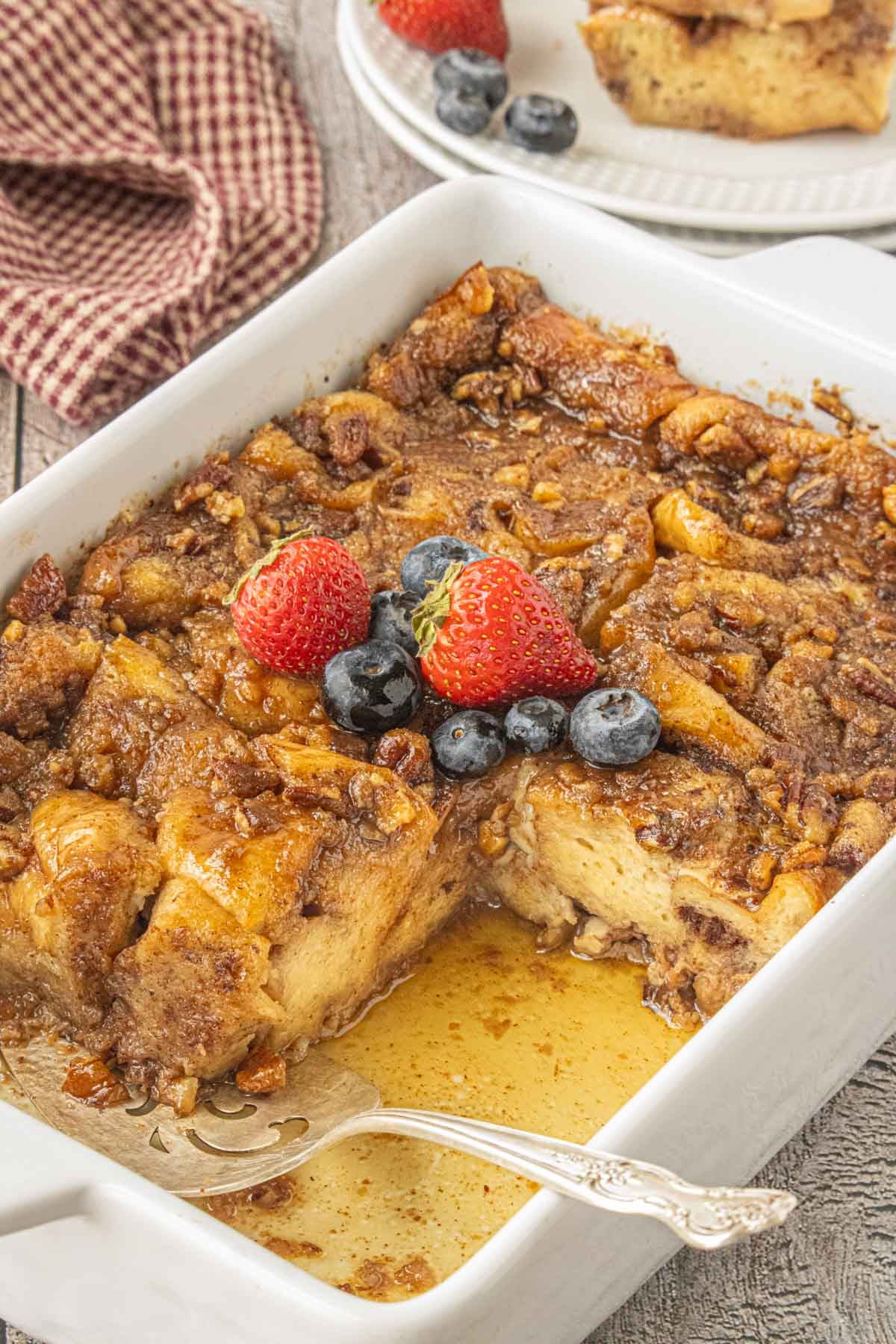 Brown Butter Praline French Toast Casserole topped with caramelized pecans and served with fresh strawberries and blueberries.