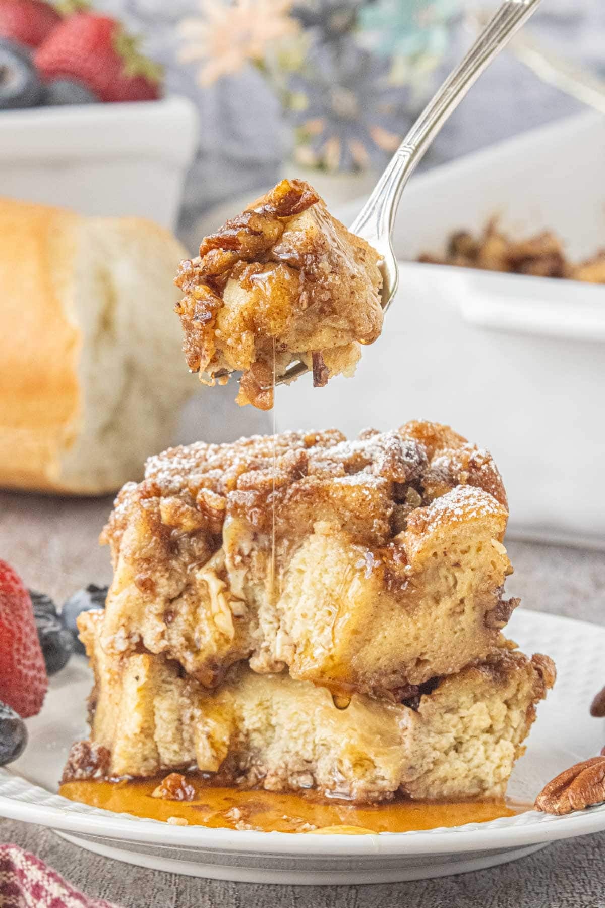 Thick slices of praline French toast casserole stacked on a plate with pecans and maple syrup.