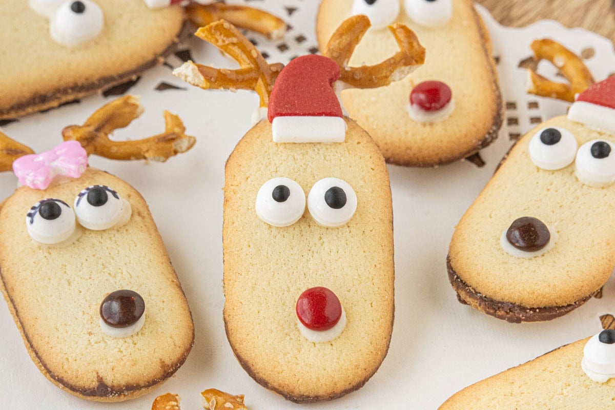 No-bake Milano reindeer cookies decorated with pretzel antlers, candy eyes, and M&M noses