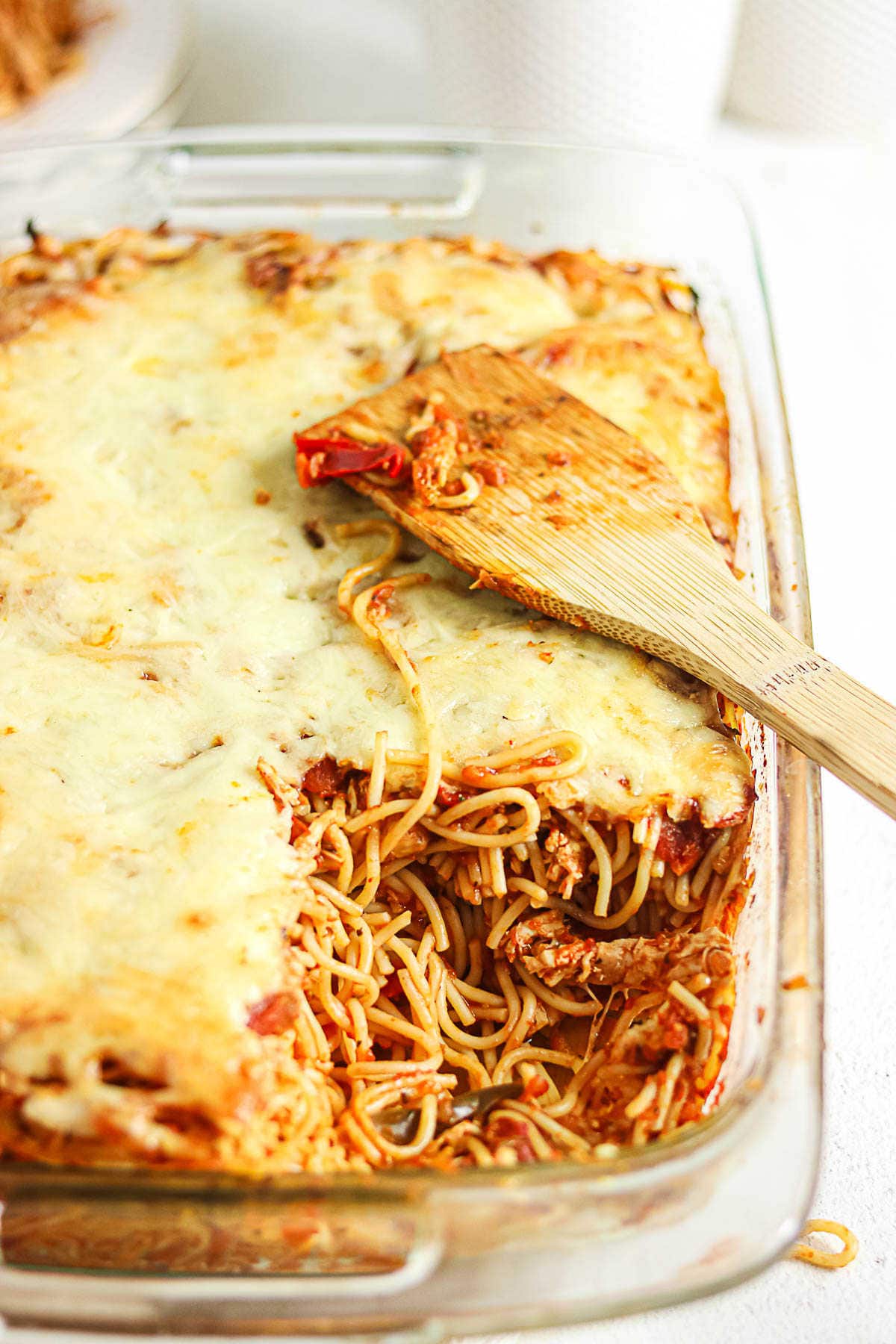 Baked chicken spaghetti with red sauce and melted cheese in a clear glass casserole dish