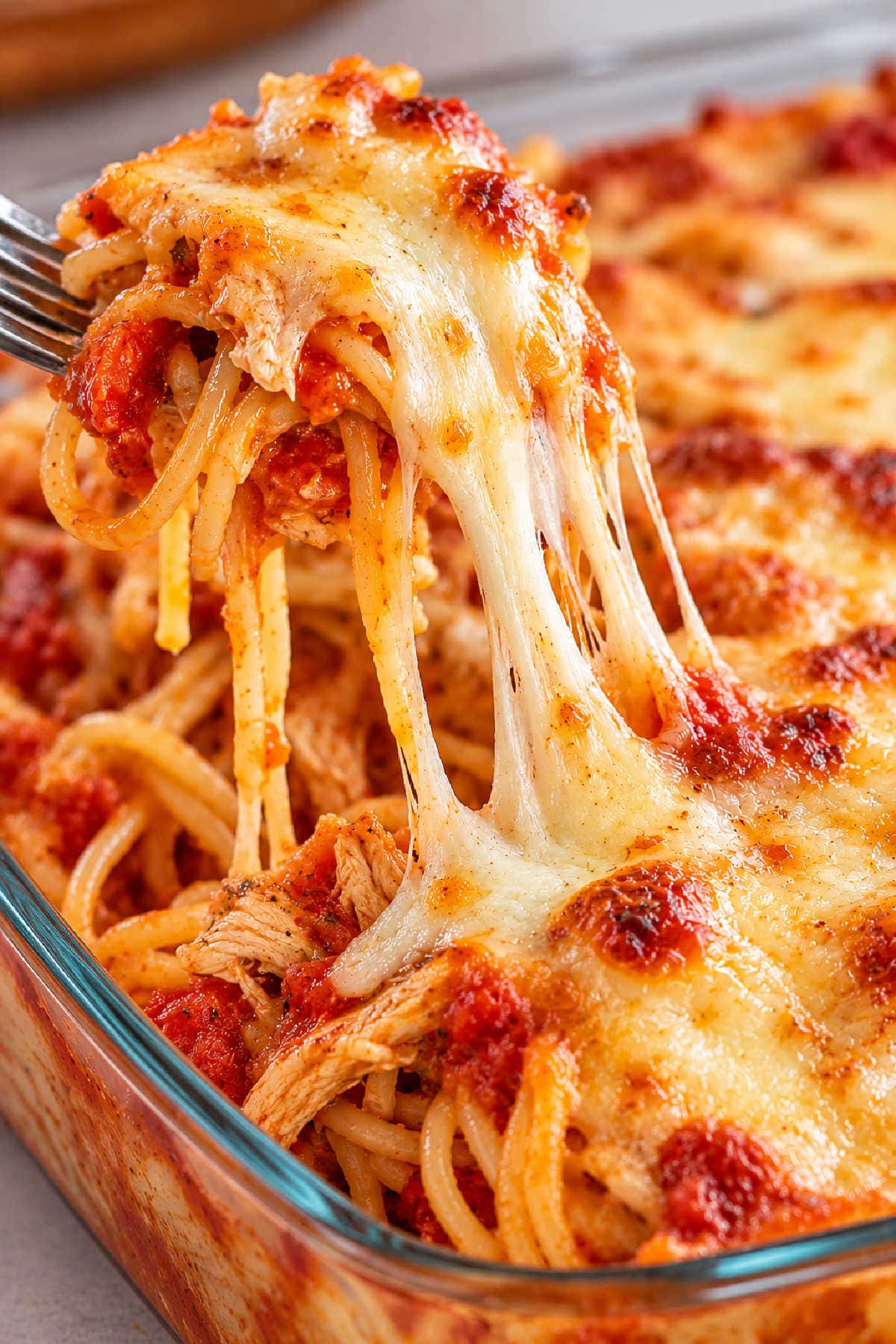 Cheesy baked chicken spaghetti with red sauce being lifted from a glass casserole dish