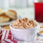 Copycat Texas Roadhouse cinnamon honey butter recipe in a white crock with biscuits in the background.