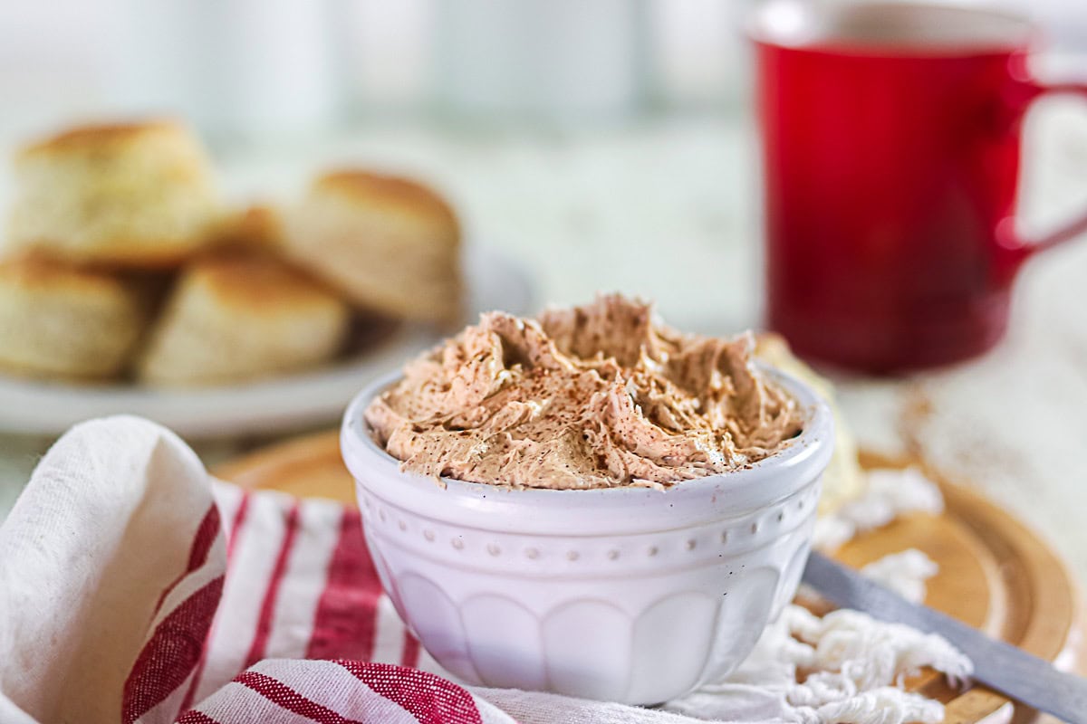 Copycat Texas Roadhouse cinnamon honey butter recipe in a white crock with biscuits in the background.
