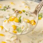 Creamy Hatch chile corn chowder with roasted corn, green chiles, and cilantro on a spoon over a bowl of chowder.
