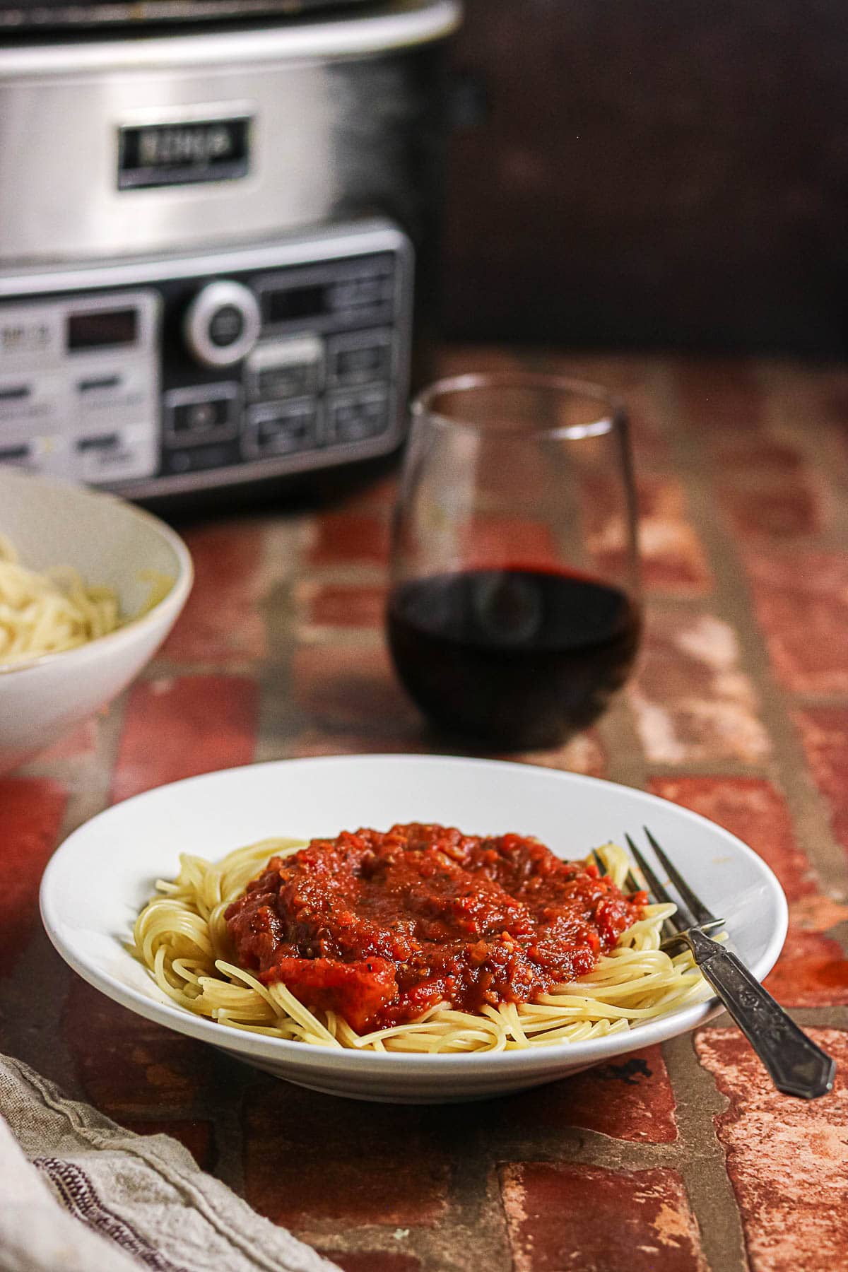 Spaghetti topped with homemade meat sauce with a slow cooker in the background.