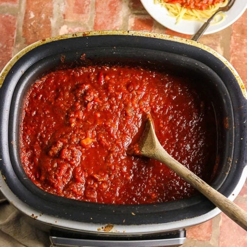 Thick homemade spaghetti sauce in a slow cooker with a wooden spoon.