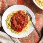 Overhead view of spaghetti with slow cooker meat sauce, cooked pasta, and serving spoon.