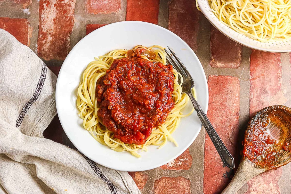 Overhead view of spaghetti with slow cooker meat sauce, cooked pasta, and serving spoon.
