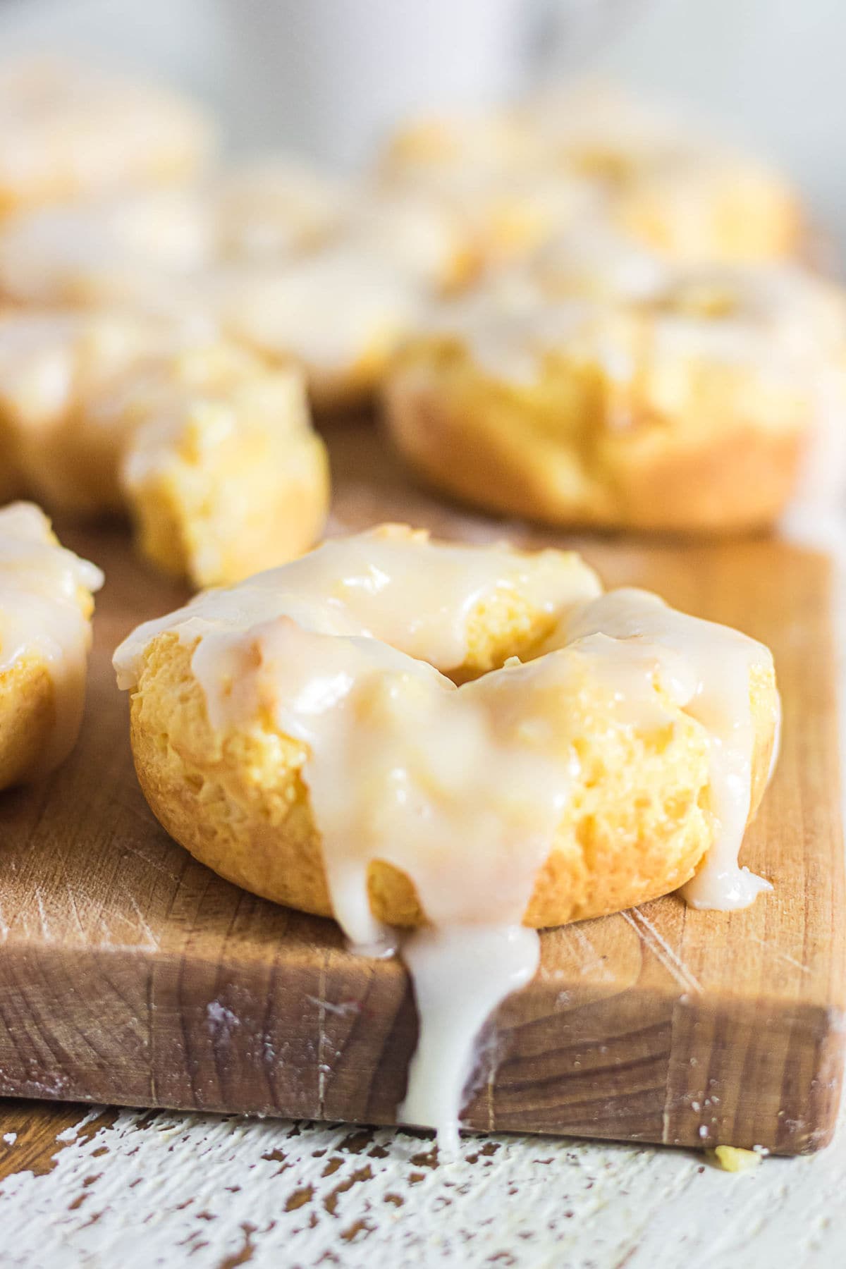 Glazed sour cream baked donut on a wooden cutting board with vanilla glaze dripping down the sides.
