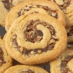 Golden brown date nut pinwheel cookies with spirals of chopped dates and pecans piled together.
