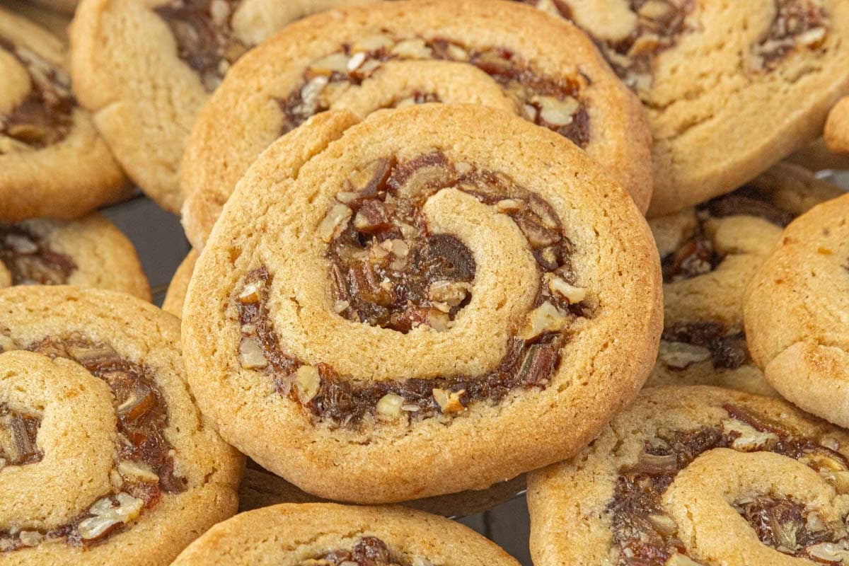 Golden brown date nut pinwheel cookies with spirals of chopped dates and pecans piled together.