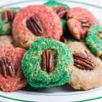 Homemade Christmas butter cookies rolled in red and green sparkling sugar and topped with pecan halves on a white platter.