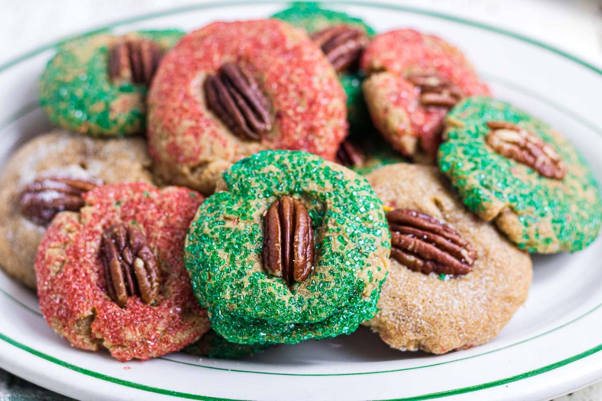 Homemade Christmas butter cookies rolled in red and green sparkling sugar and topped with pecan halves on a white platter.
