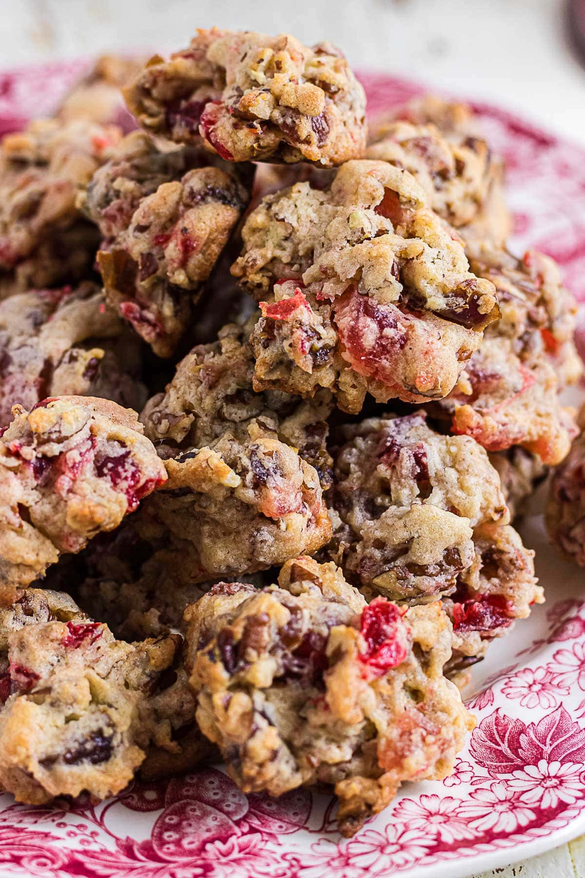 Close-up of old-fashioned fruitcake cookies packed with candied cherries, pineapple, dates, and pecans on a red transferware plate.