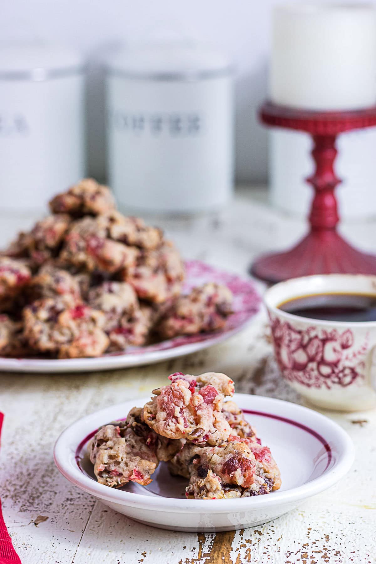 Homemade Christmas fruitcake cookies on a small white plate with a vintage red transferware coffee cup and more cookies in the background.