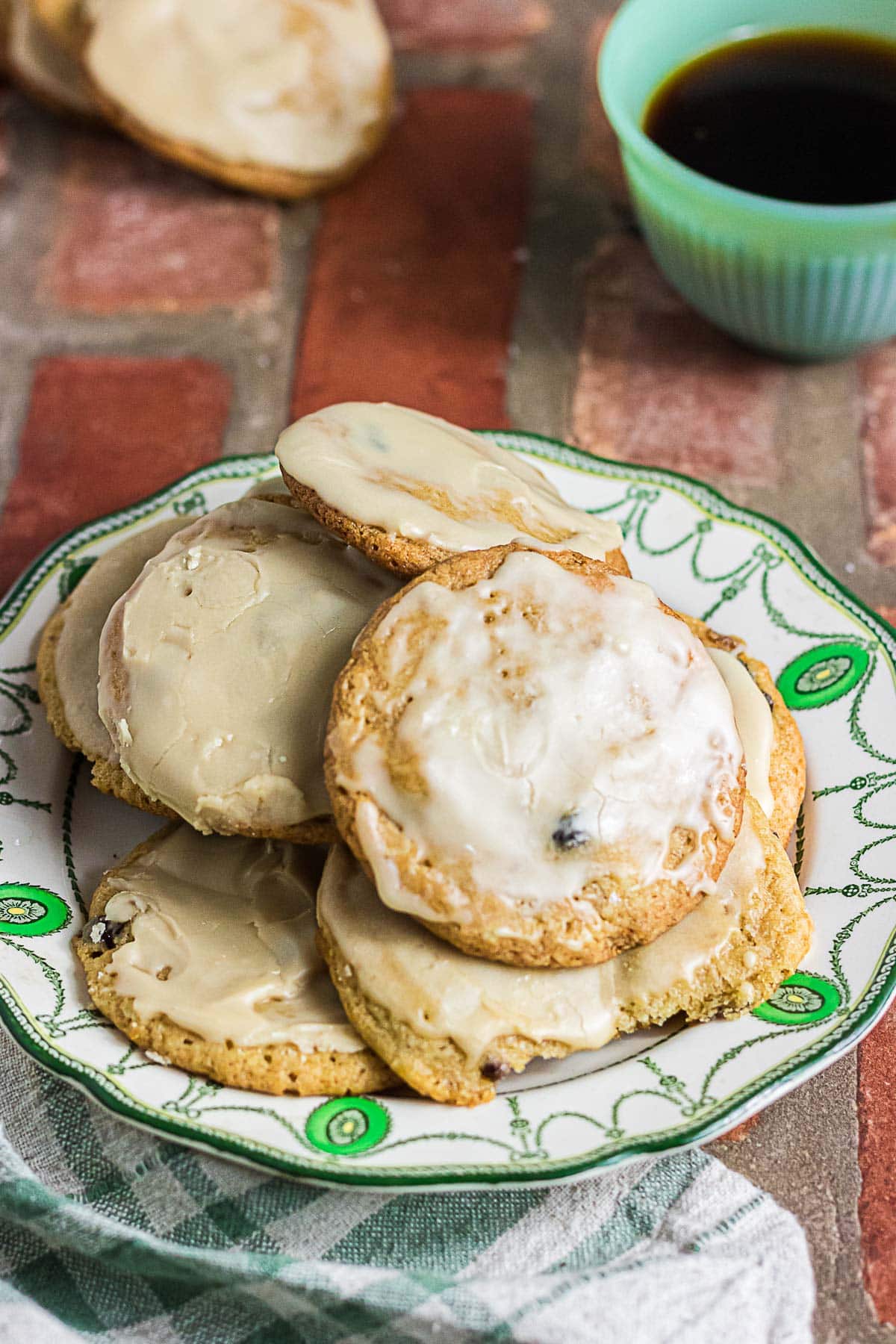 Homemade mincemeat cookies with coffee glaze piled on a vintage green and white plate beside a cup of coffee.