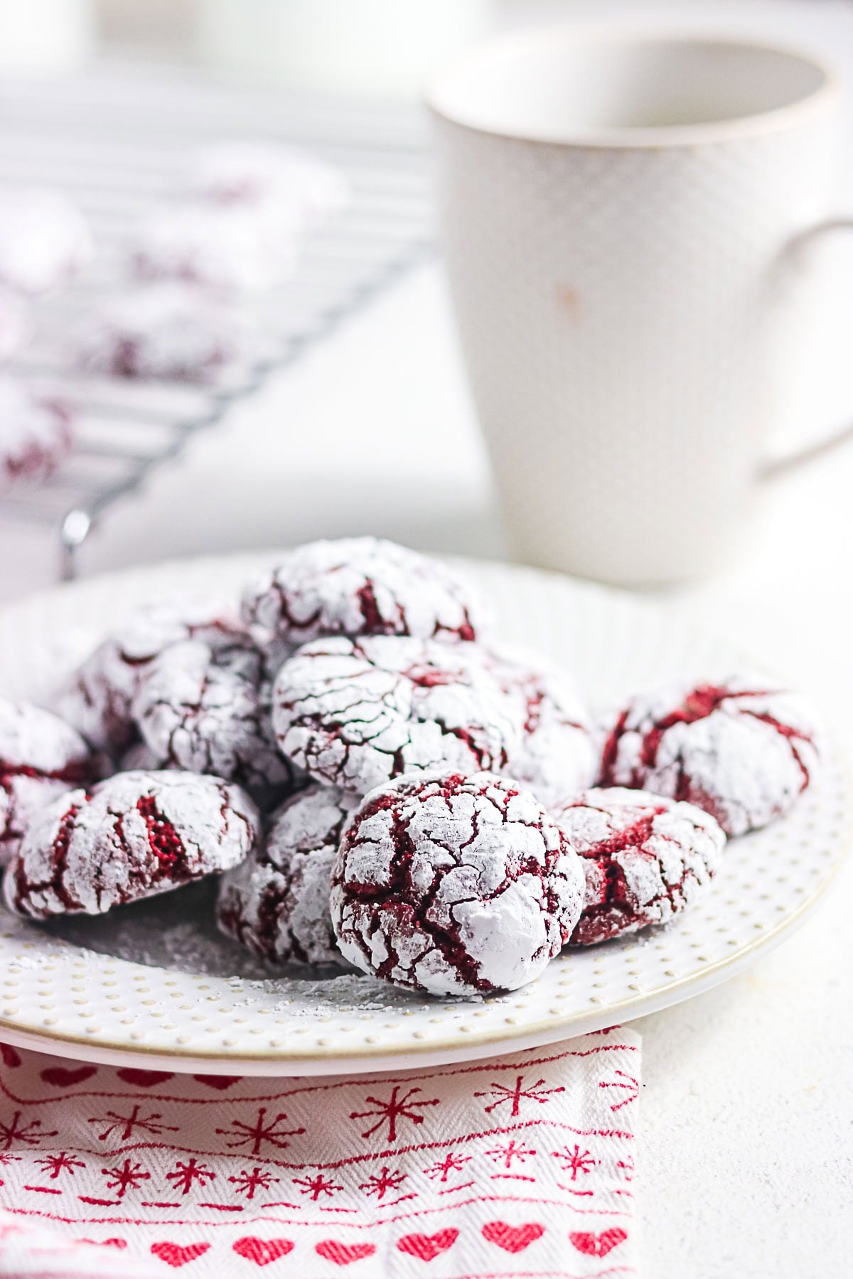 Plate of powdered sugar red velvet crinkle cookies with a coffee mug
