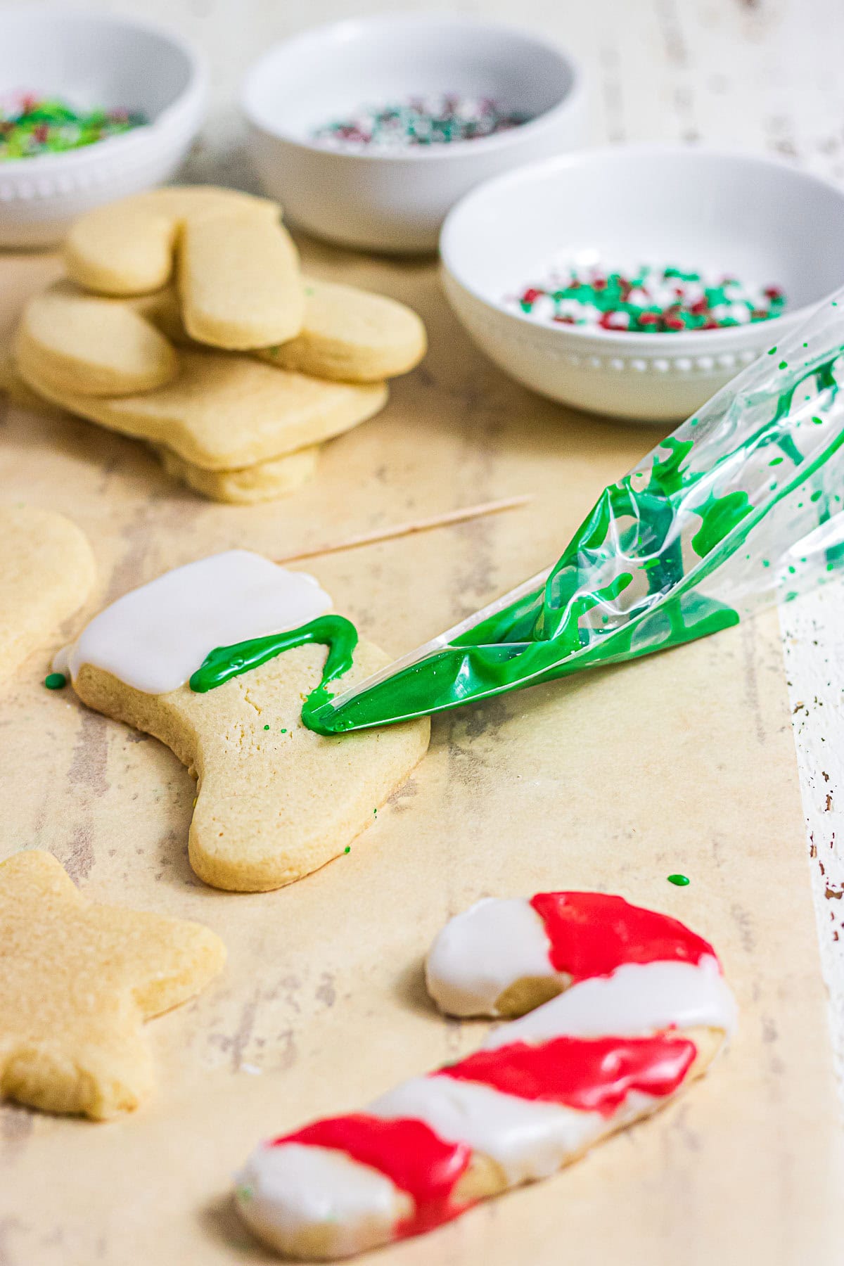 Piping green sugar cookie glaze onto a Christmas stocking cookie with decorated candy cane cookies nearby