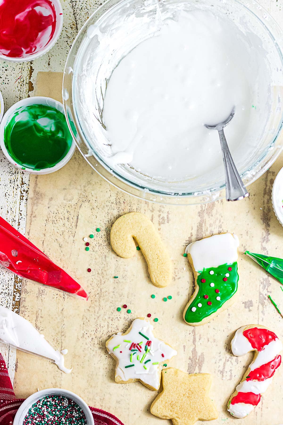 Overhead view of white sugar cookie glaze with red and green icing, piping bags, and Christmas cutout cookies