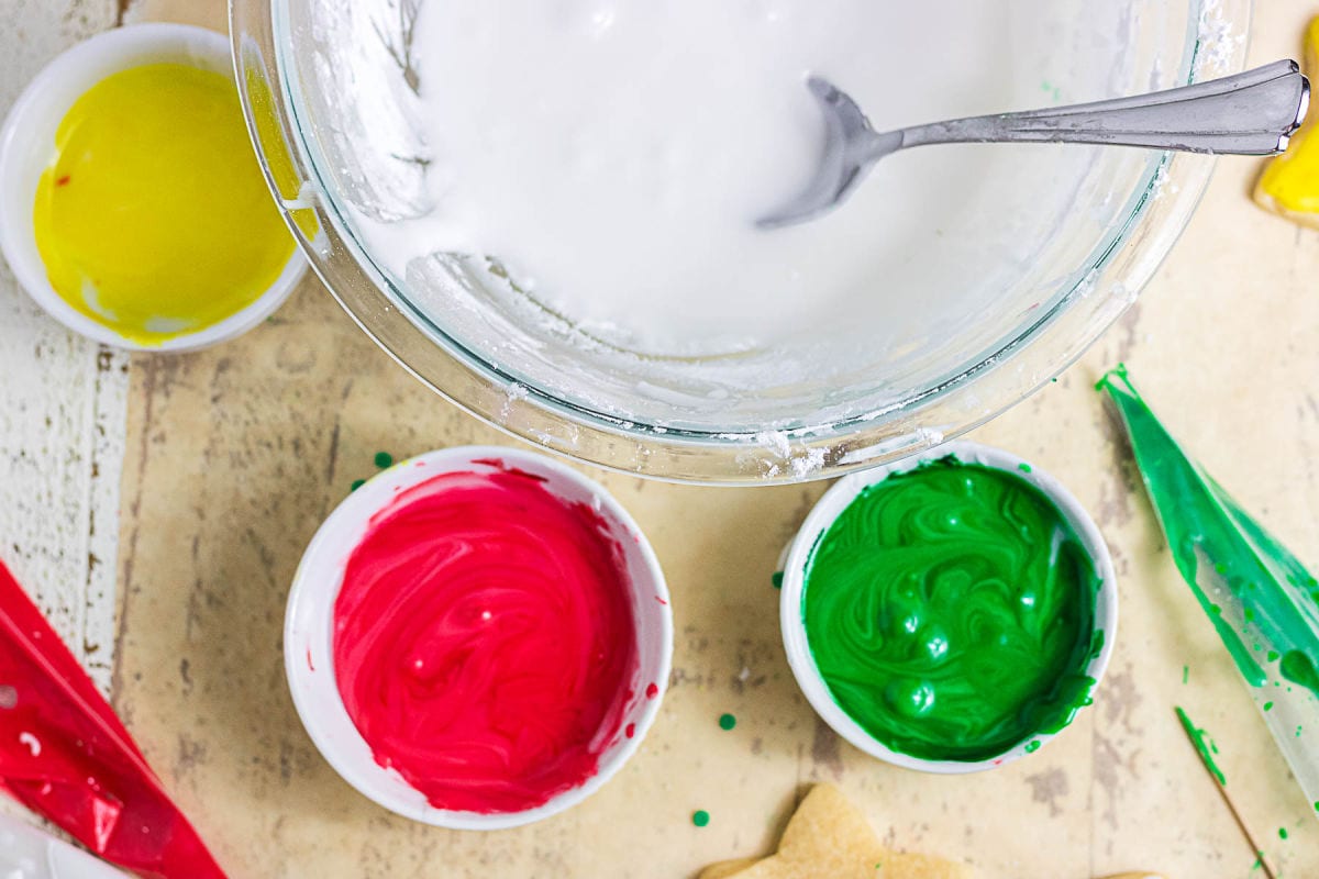 Homemade sugar cookie glaze in white, yellow, red, and green with piping bags.