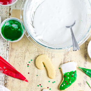 Easy sugar cookie glaze in a mixing bowl with red and green icing and Christmas cutout cookies ready to decorate
