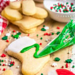 Christmas sugar cookie glaze Pinterest pin showing green icing piped onto a stocking-shaped cookie, a red and white candy cane cookie, and festive sprinkles.